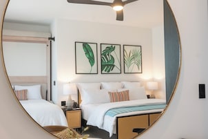 Habitación de hotel con cama, dos mesitas de noche, un espejo y tres cuadros con hojas enmarcadas en la pared.