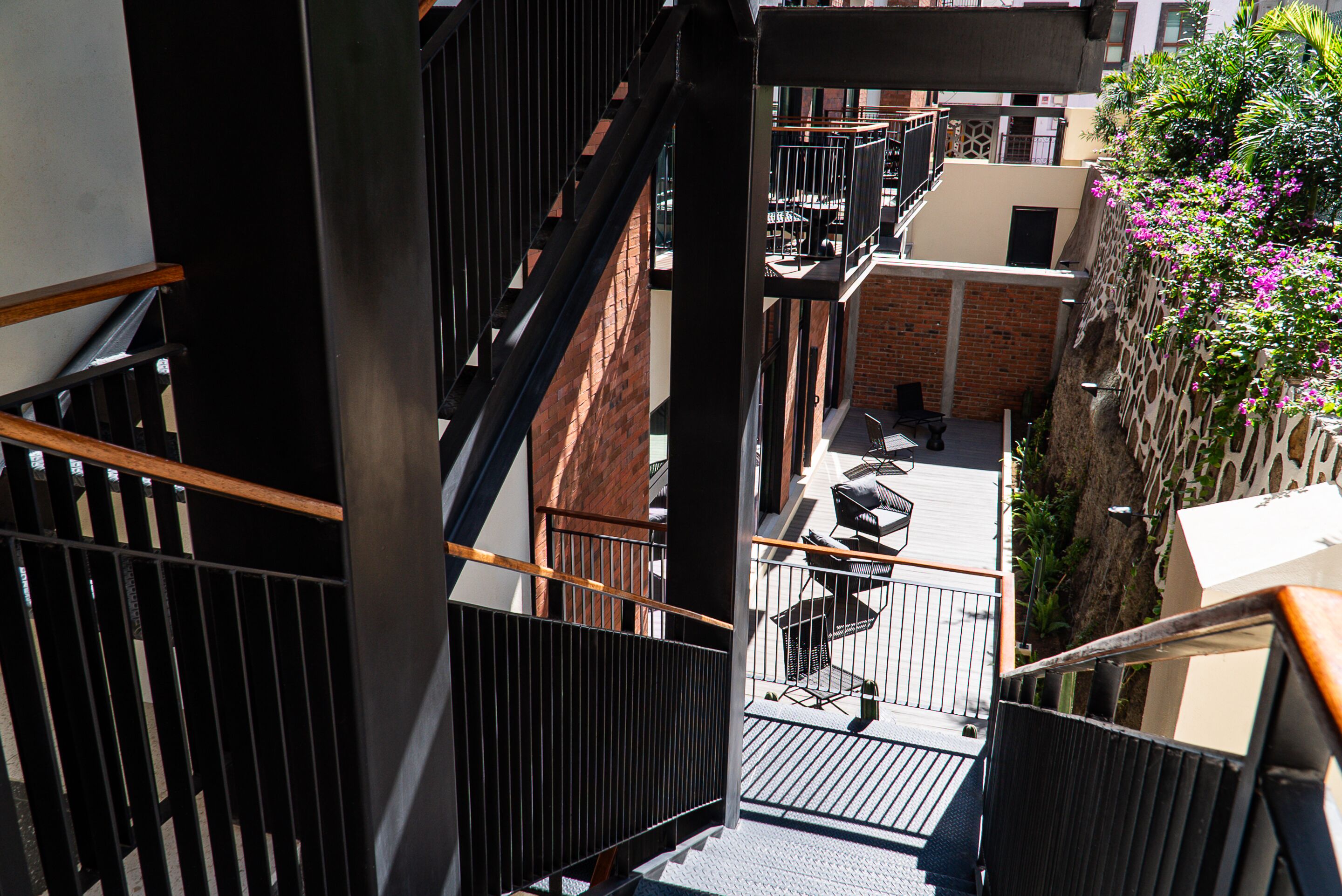 Vista desde un balcón sobre un patio con mesas al aire libre y una escalera.