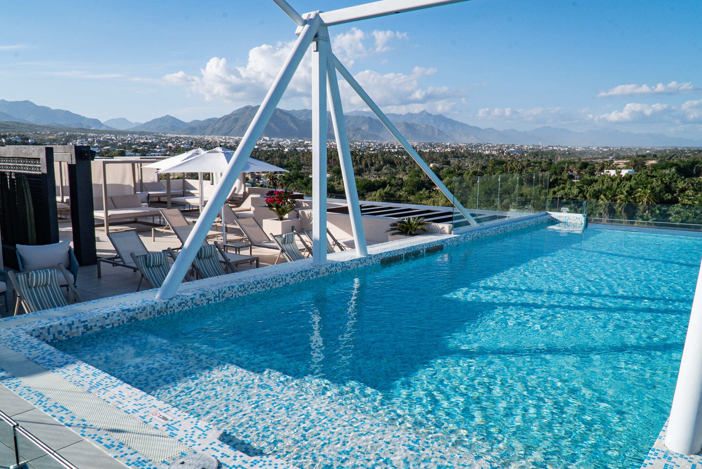 A rooftop infinity pool with a clear view of the city and mountains in the background.