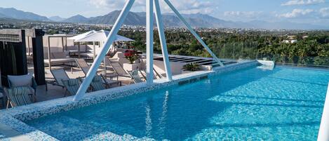 A rooftop infinity pool with a clear view of the city and mountains in the background.