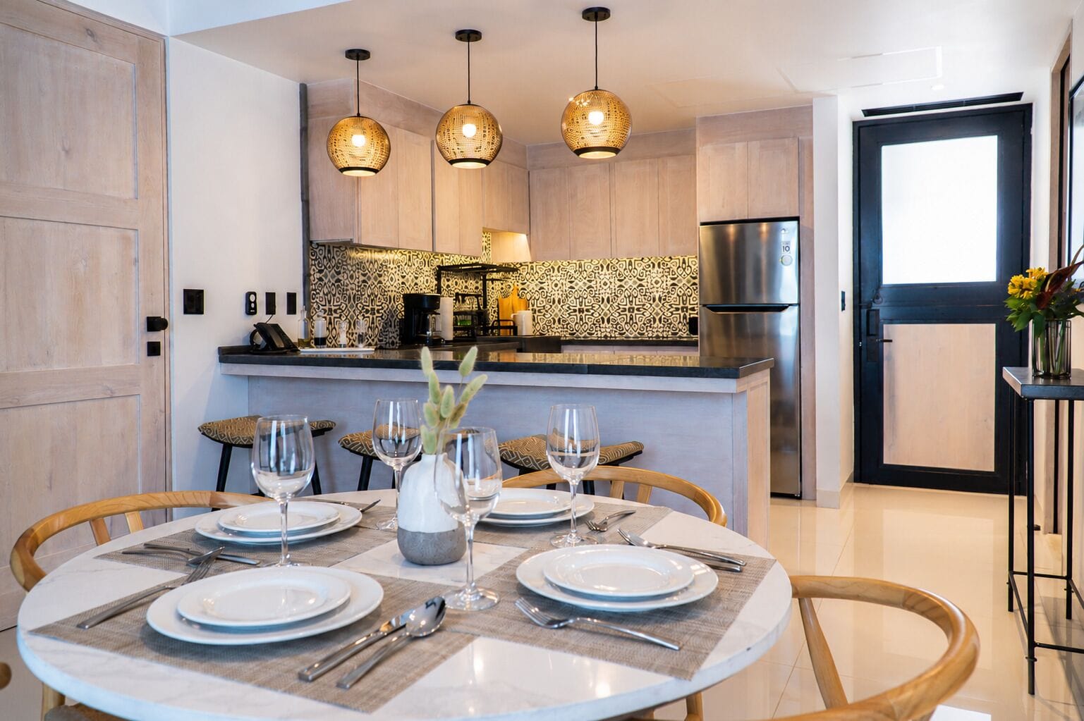 Una cocina moderna con una isla central, luces colgantes y un comedor con una mesa redonda dispuesta para cuatro.