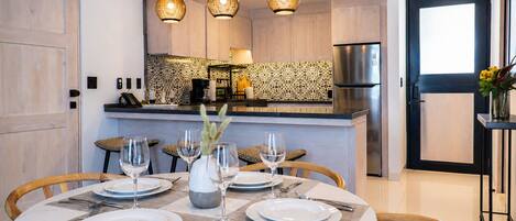 Una cocina moderna con una isla central, luces colgantes y un comedor con una mesa redonda dispuesta para cuatro.