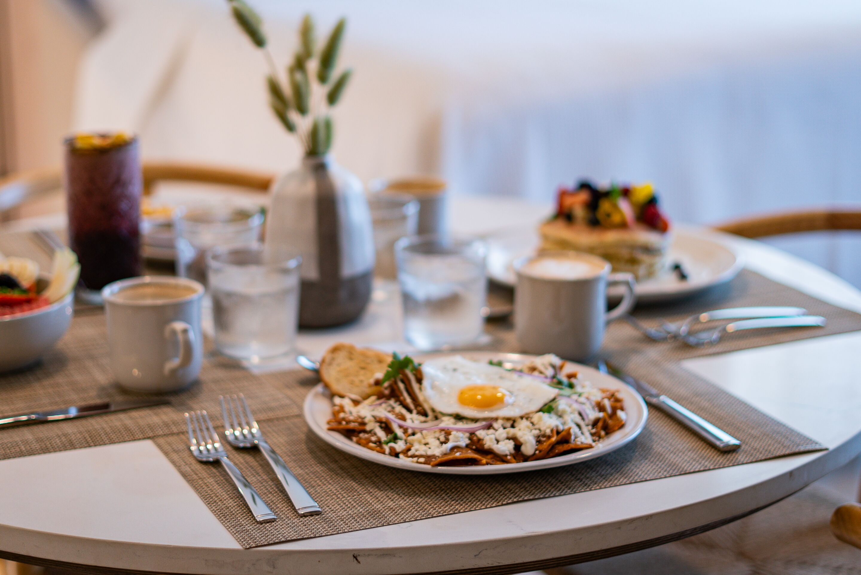 Una escena de desayuno con un plato de huevos y tostadas, una taza de café y un florero con follaje.