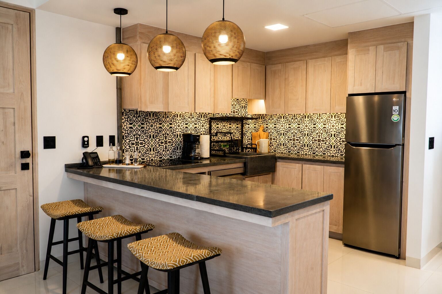 A modern kitchen with a central island, bar stools, a refrigerator, and pendant lighting.