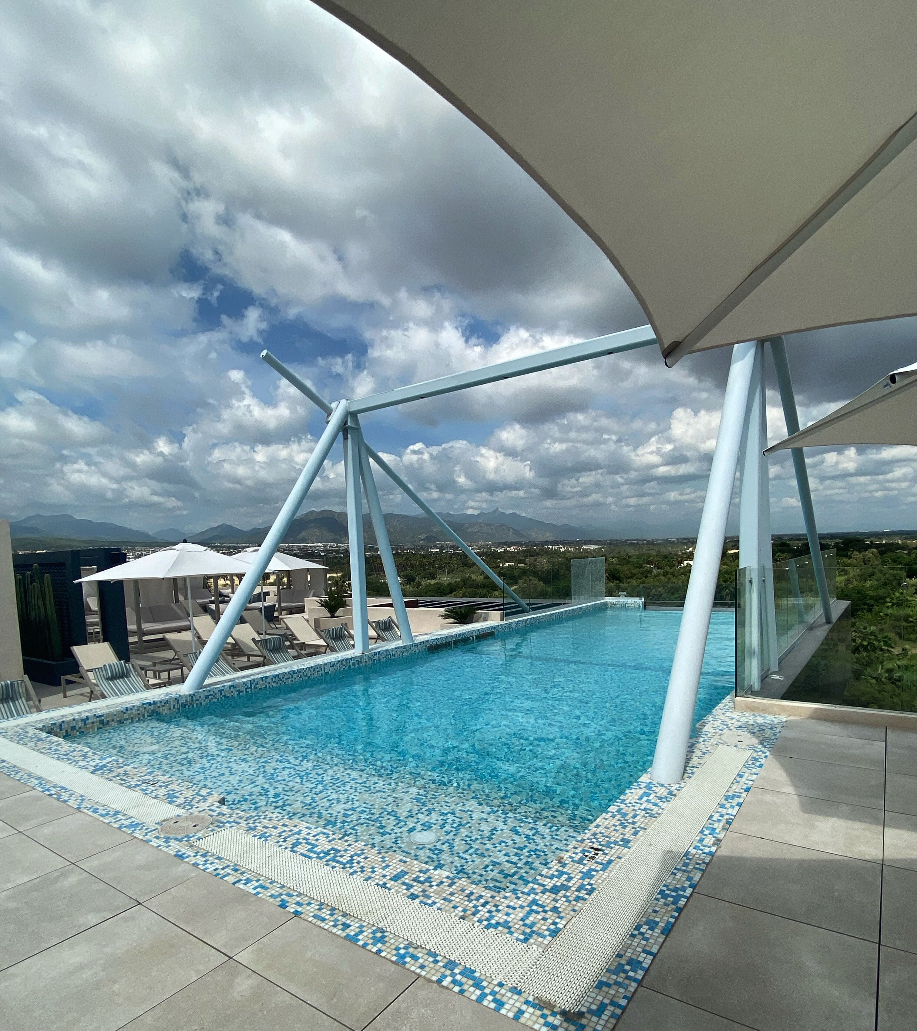 Una piscina en la azotea con vistas despejadas del paisaje circundante, incluyendo montañas y el perfil del horizonte urbano.