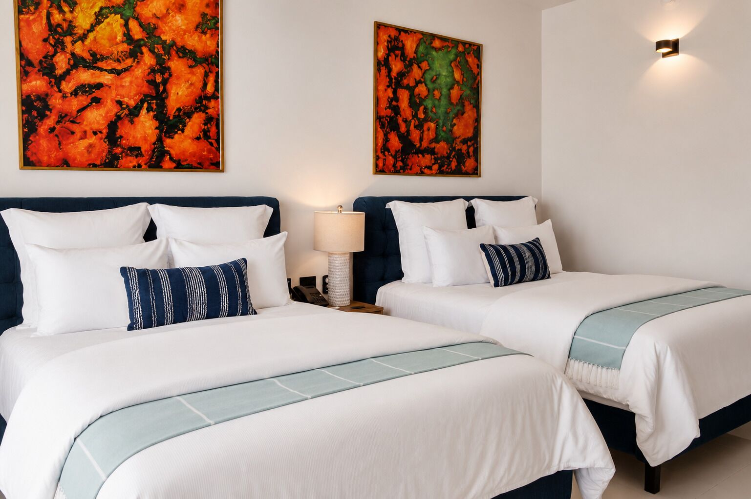 A hotel room with two beds, white bedding, and two abstract paintings on the wall.