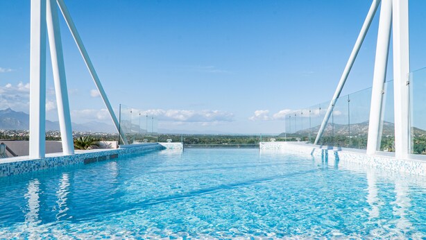 Piscina azul cristalina con pilares blancos y vistas a montañas distantes.
