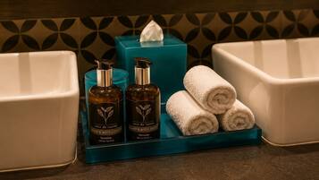 A bathroom vanity with a blue soap dish, two bottles of hand and body wash, and three rolled towels.