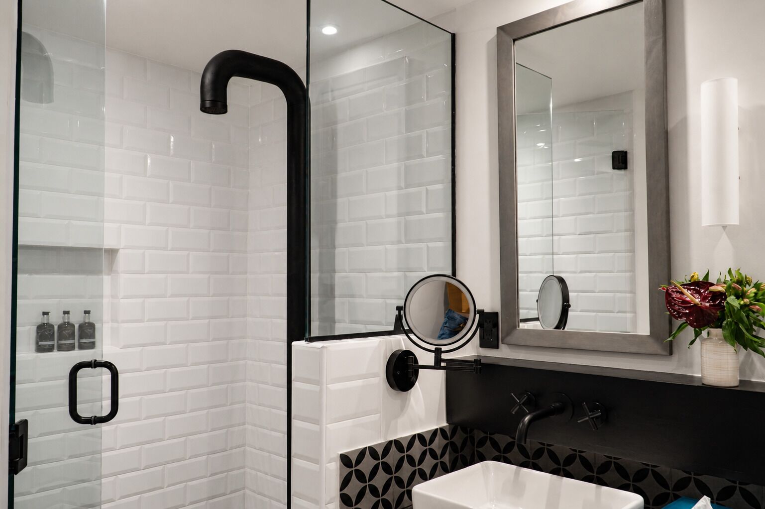 A modern bathroom with a glass-enclosed shower, a large mirror, and a white sink with a black patterned backsplash.