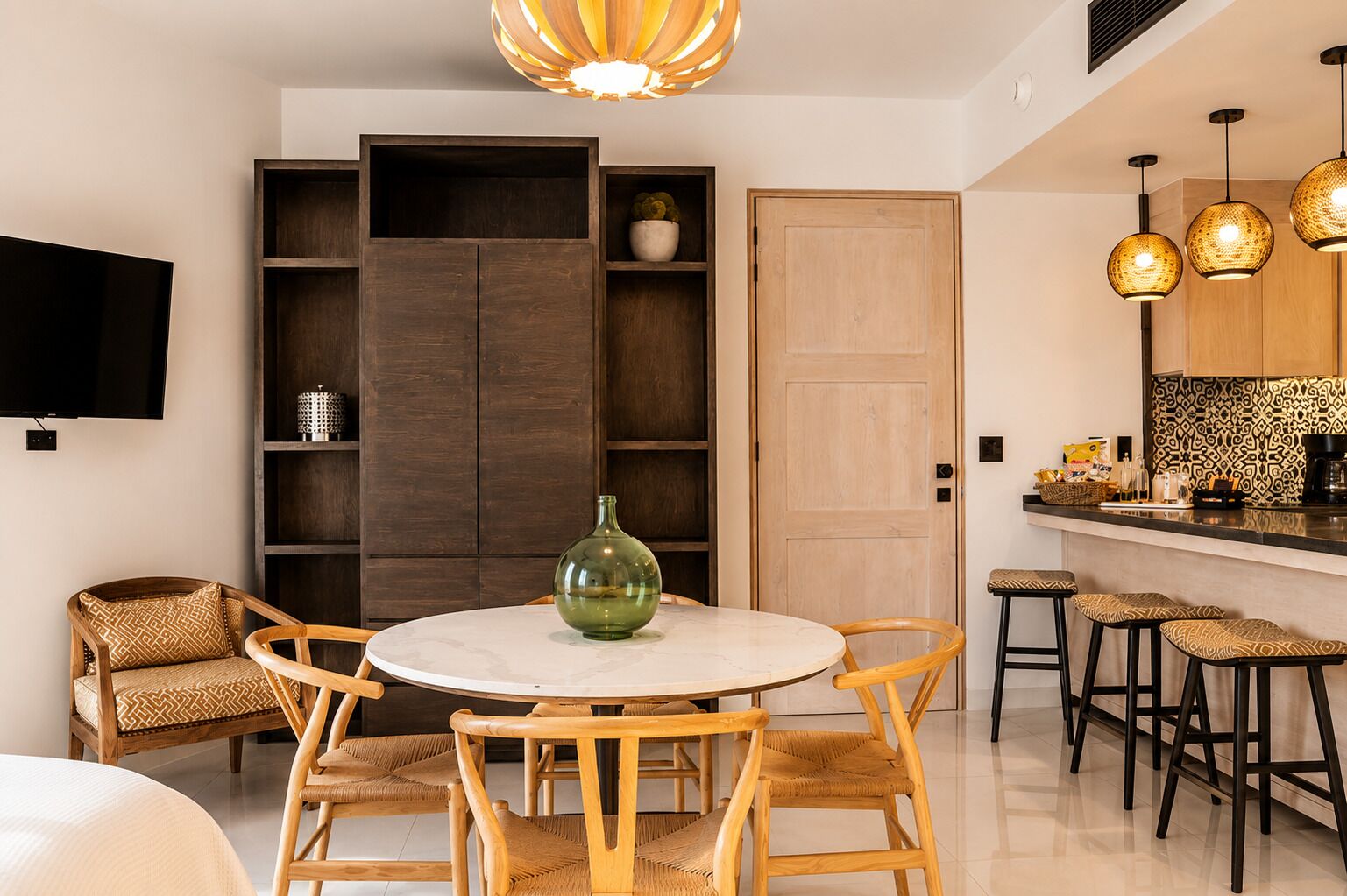 A modern kitchen with a round dining table, wooden chairs, and pendant lighting.