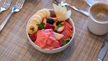 A bowl of fruit salad with strawberries, bananas, and blueberries, accompanied by a cup of coffee on a table with a placemat.