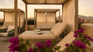 A rooftop lounge area with multiple seating options, including lounge chairs and a sofa, under a canopy.