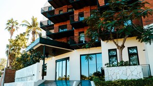 Un edificio moderno con fachada de piedra, varios balcones y una palmera al frente.