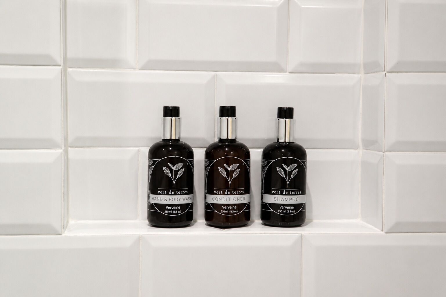 Three bottles of Verveine products on a white tiled shelf.