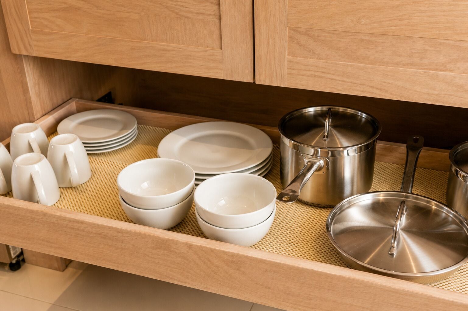 A kitchen drawer with various white ceramic dishes, including bowls and mugs, and stainless steel cookware.