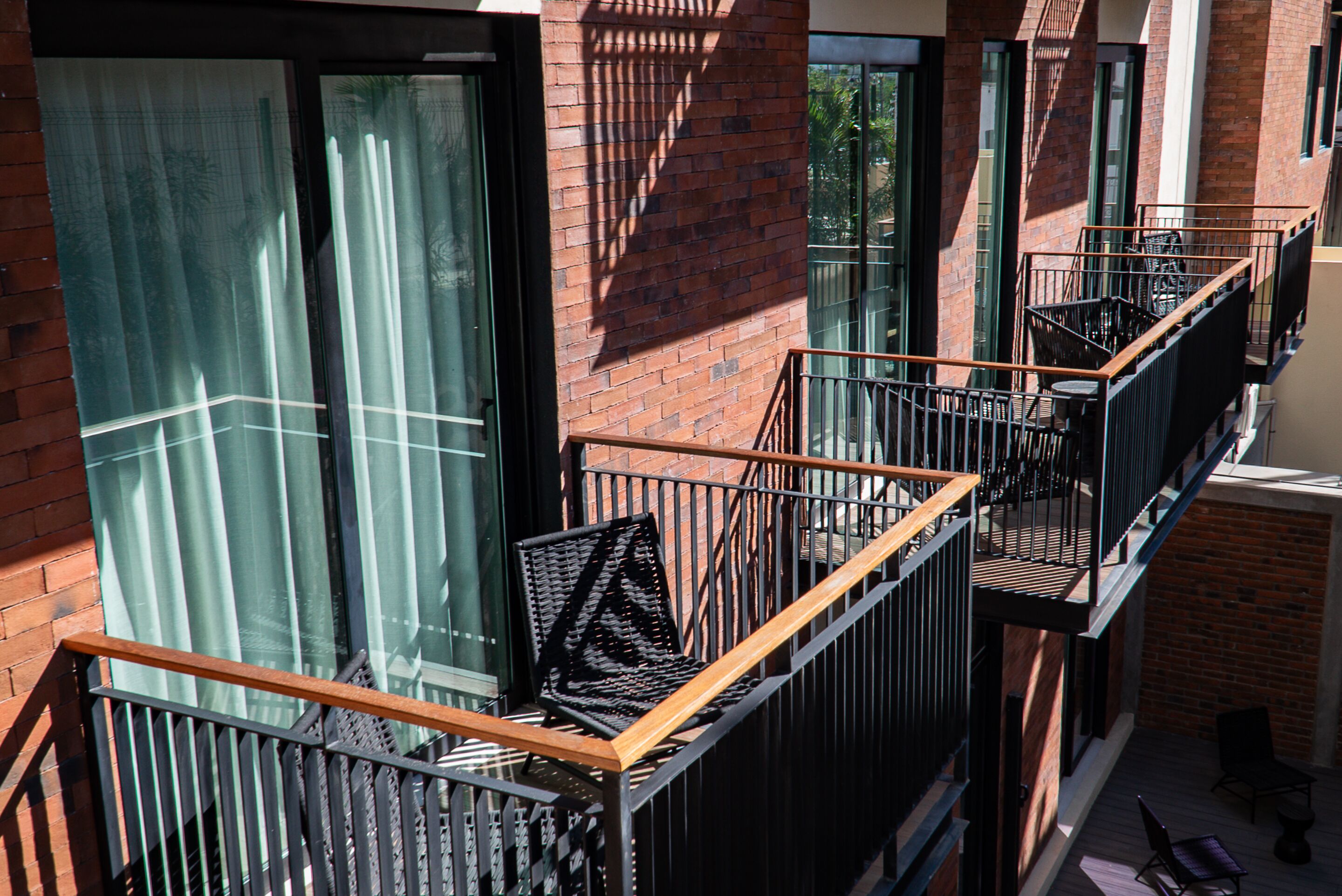 A multi-story building with a brick facade, large windows, and a balcony with metal railings and a wooden bench.
