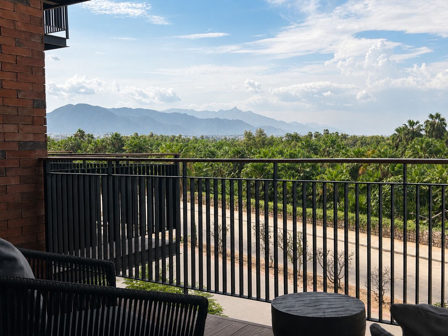 A balcony with a view of a mountain range and a palm tree-lined street.