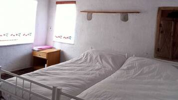 A single-bed room with a wooden ceiling, a small bedside table, and a window with floral curtains.