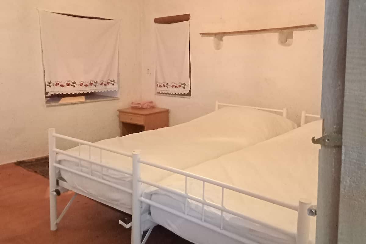 Une chambre avec un lit simple, un plafond en bois, des murs blancs et une petite table de chevet.