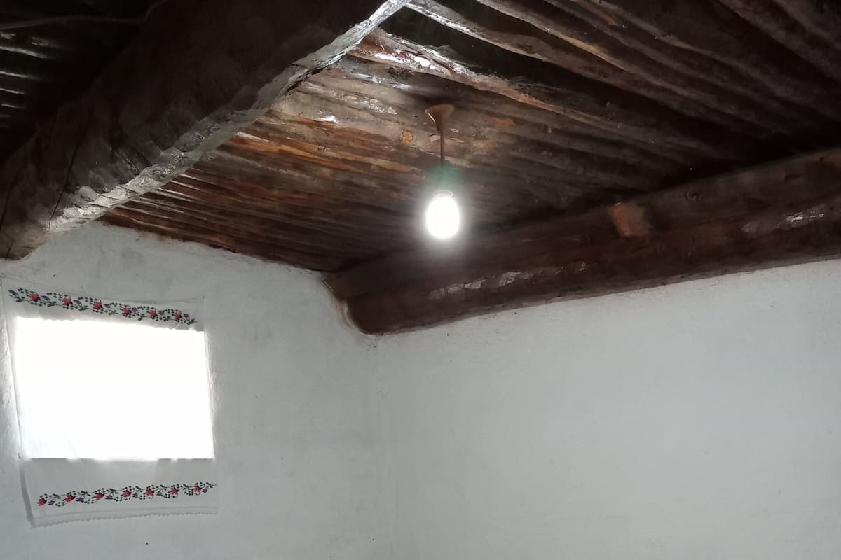 Une chambre avec deux lits simples, une petite table de chevet en bois, une fenêtre ornée d’un motif décoratif et un plafond en pente avec des poutres apparentes.