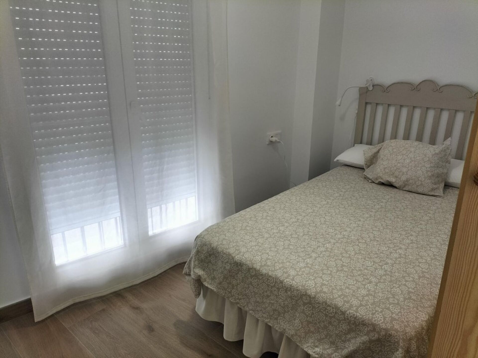 A bedroom with a bed, a window with blinds, and a door.