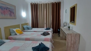 Ein Hotelzimmer mit zwei Betten, einem Holzkoffer, einem Spiegel, einem Ventilator und einem Gemälde an der Wand.