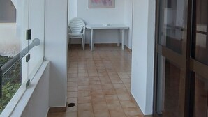 Ein Korridor mit gefliestem Boden, einer weißen Wand mit einem Gemälde, einem weißen Tisch mit einem Stuhl und einer Glastür.