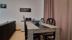 Ein gemütlicher Wohnraum mit Küchenzeile, einem Esstisch mit Stühlen, einer Couch und einem Vorhang.