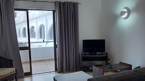 Ein modernes Wohnzimmer mit einer Couch, einem Flachbildfernseher und einem Balkon mit Vorhängen.