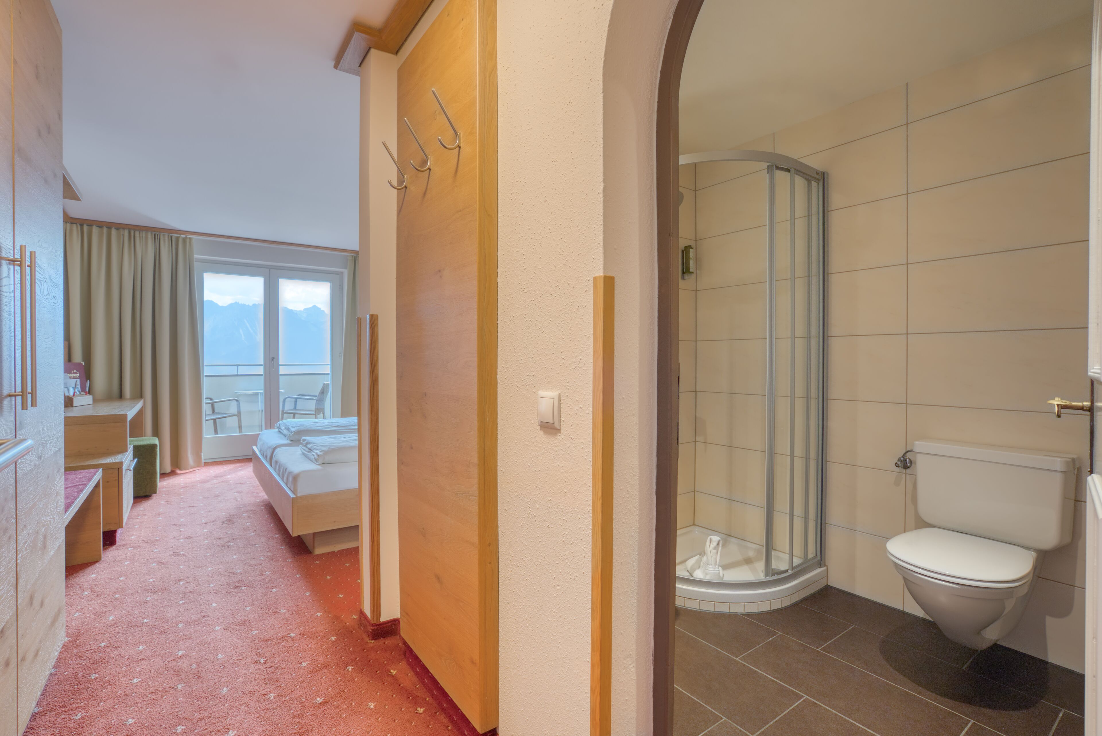 A hotel room with a bed, a bathroom with a toilet and shower, and a view of mountains through a window.