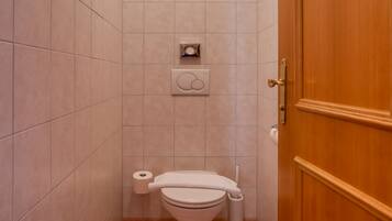 Een kleine badkamer met een toilet, een prullenbak en een handdoekhouder.