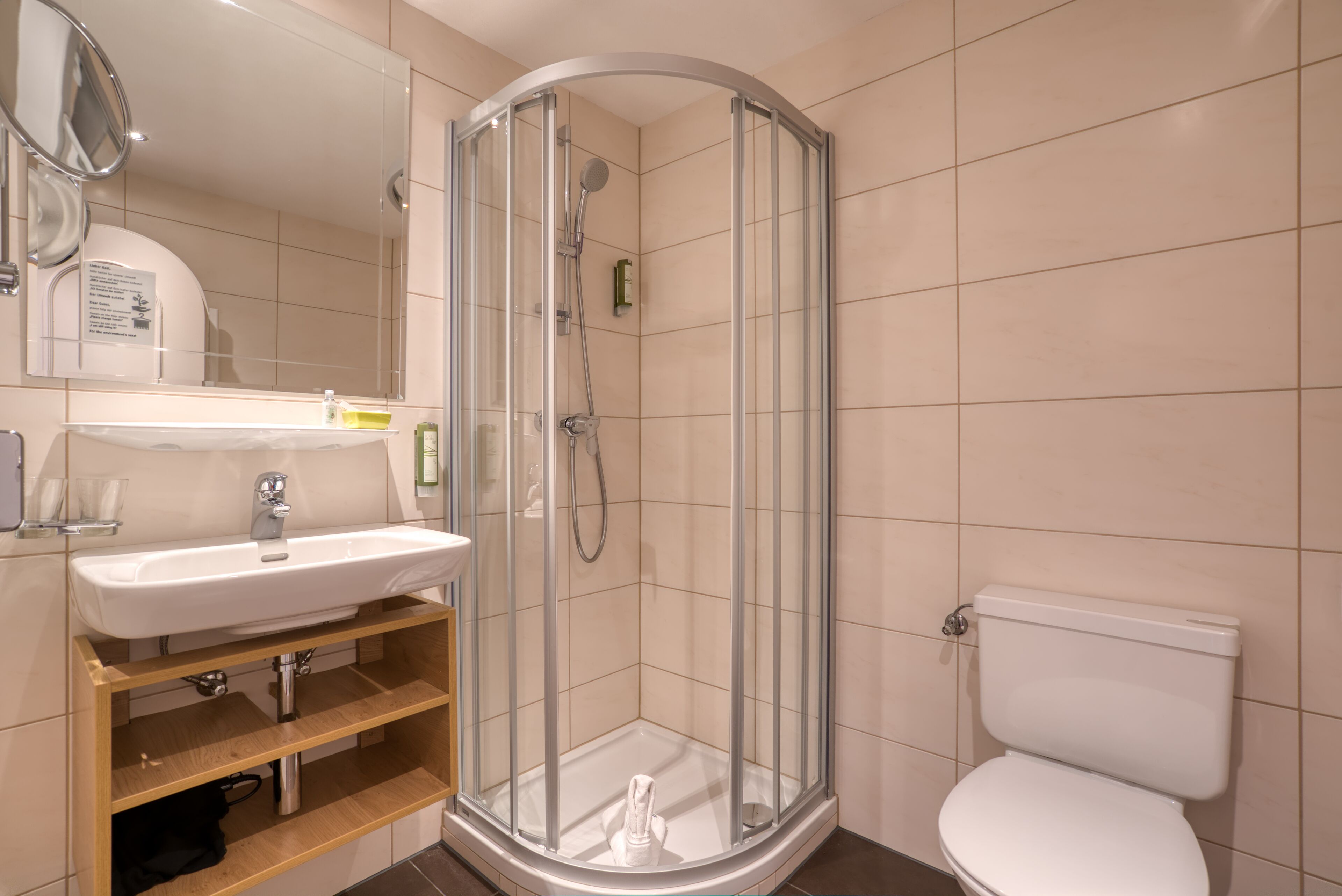 Et moderne badeværelse med en glasafskærmet brusekabine, et hvidt håndvaskarrangement og et toilet.