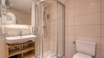 Et moderne badeværelse med en glasafskærmet brusekabine, et hvidt håndvaskarrangement og et toilet.