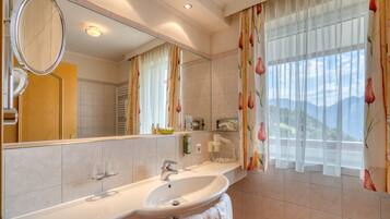 A bathroom with a large mirror, a sink, a towel rack, and a window with floral curtains.