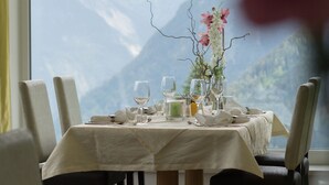Una mesa de comedor con sillas, un florero con flores y una vista de la montaña a través de una ventana.