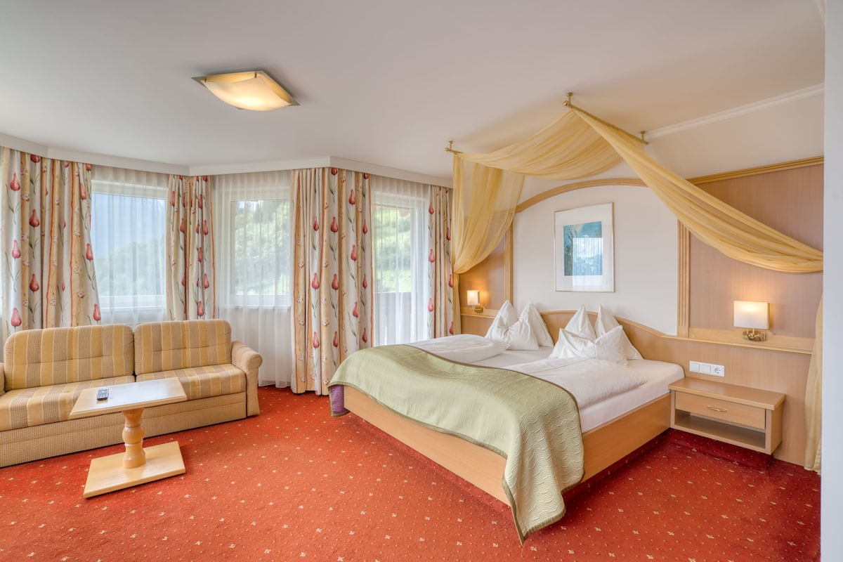 A hotel room with a bed, a sofa, a small table, and a nightstand.