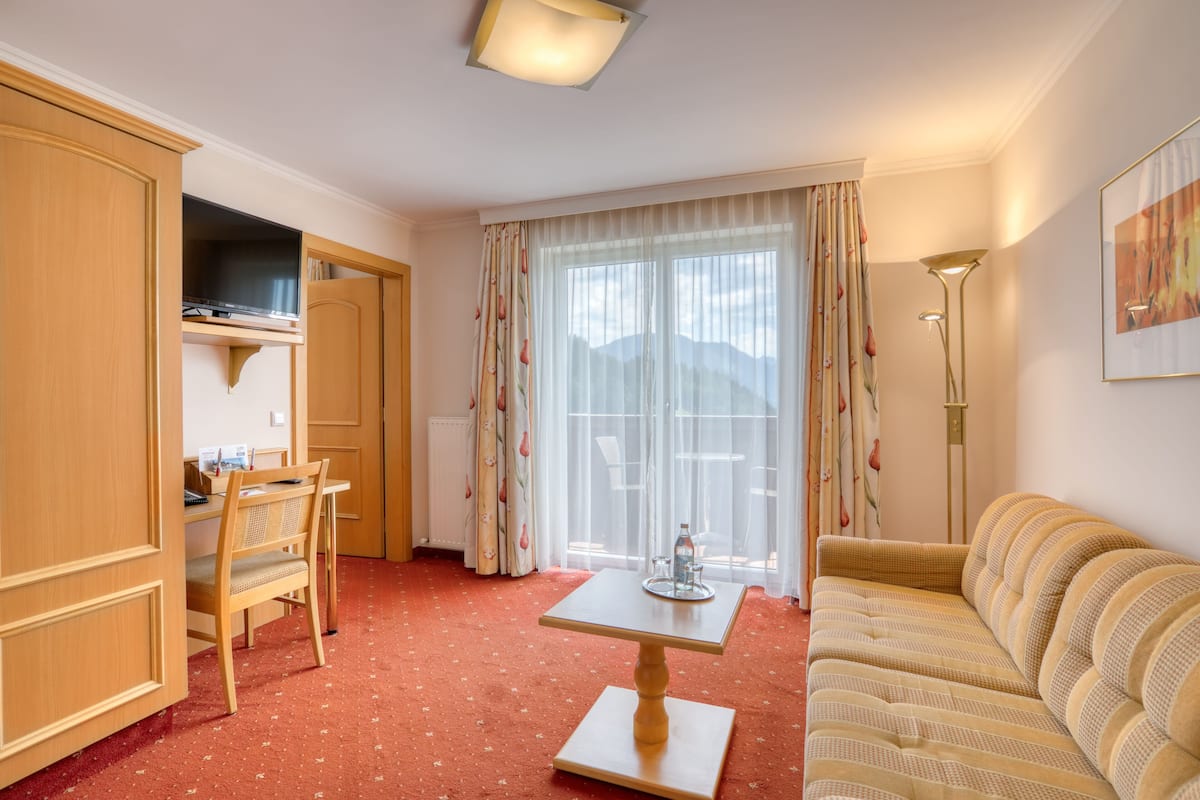 A hotel room with a wooden desk, a sofa, a TV, and a large window with curtains.