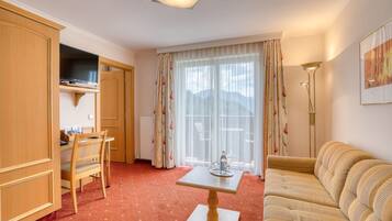Een hotelkamer met een houten bureau, een bank, een televisie en een groot raam met gordijnen.