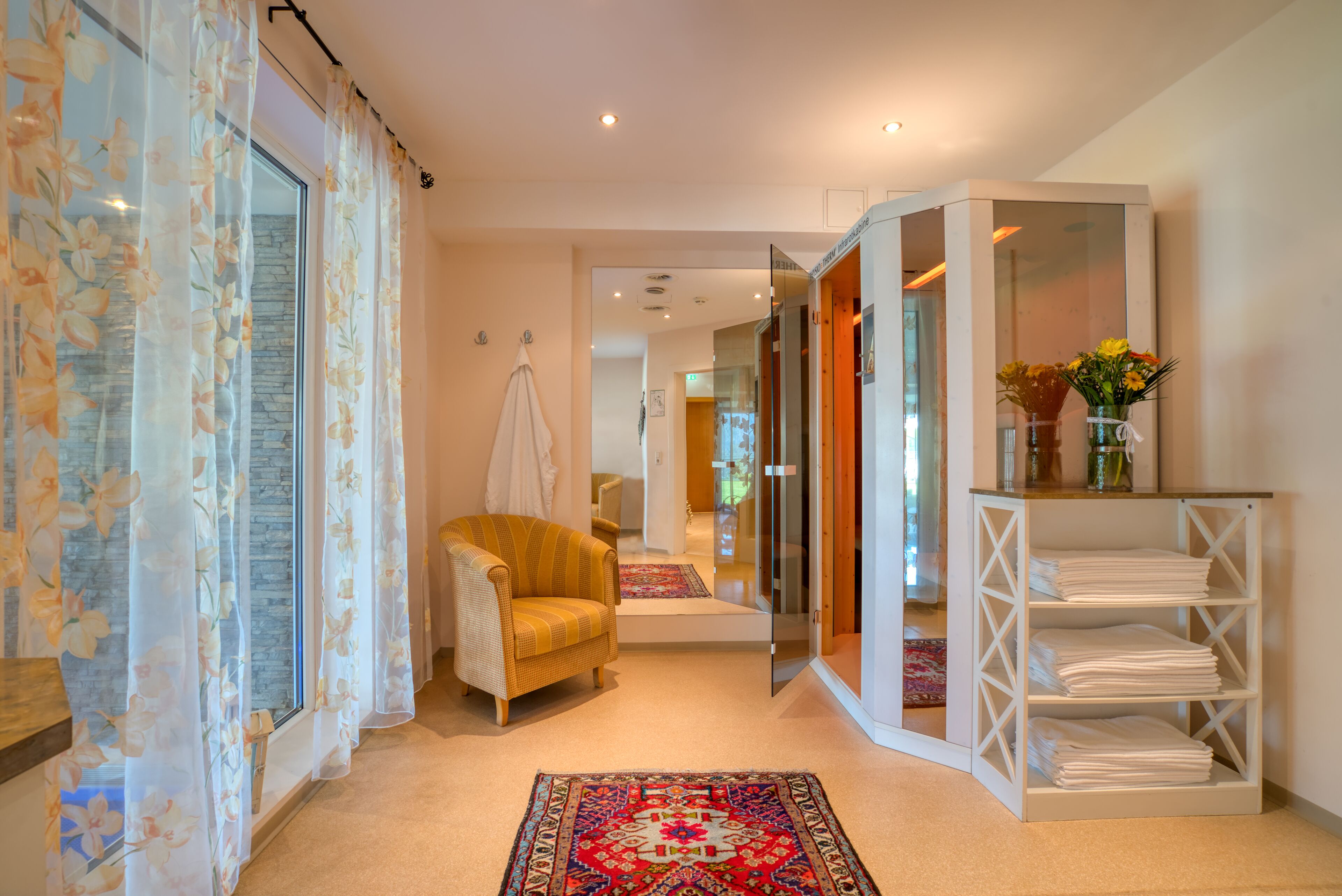 A hallway with a yellow armchair, a white shelf with folded towels, and a patterned rug.