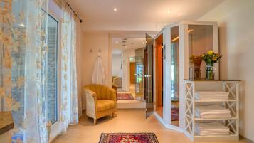 A hallway with a yellow armchair, a white shelf with folded towels, and a patterned rug.