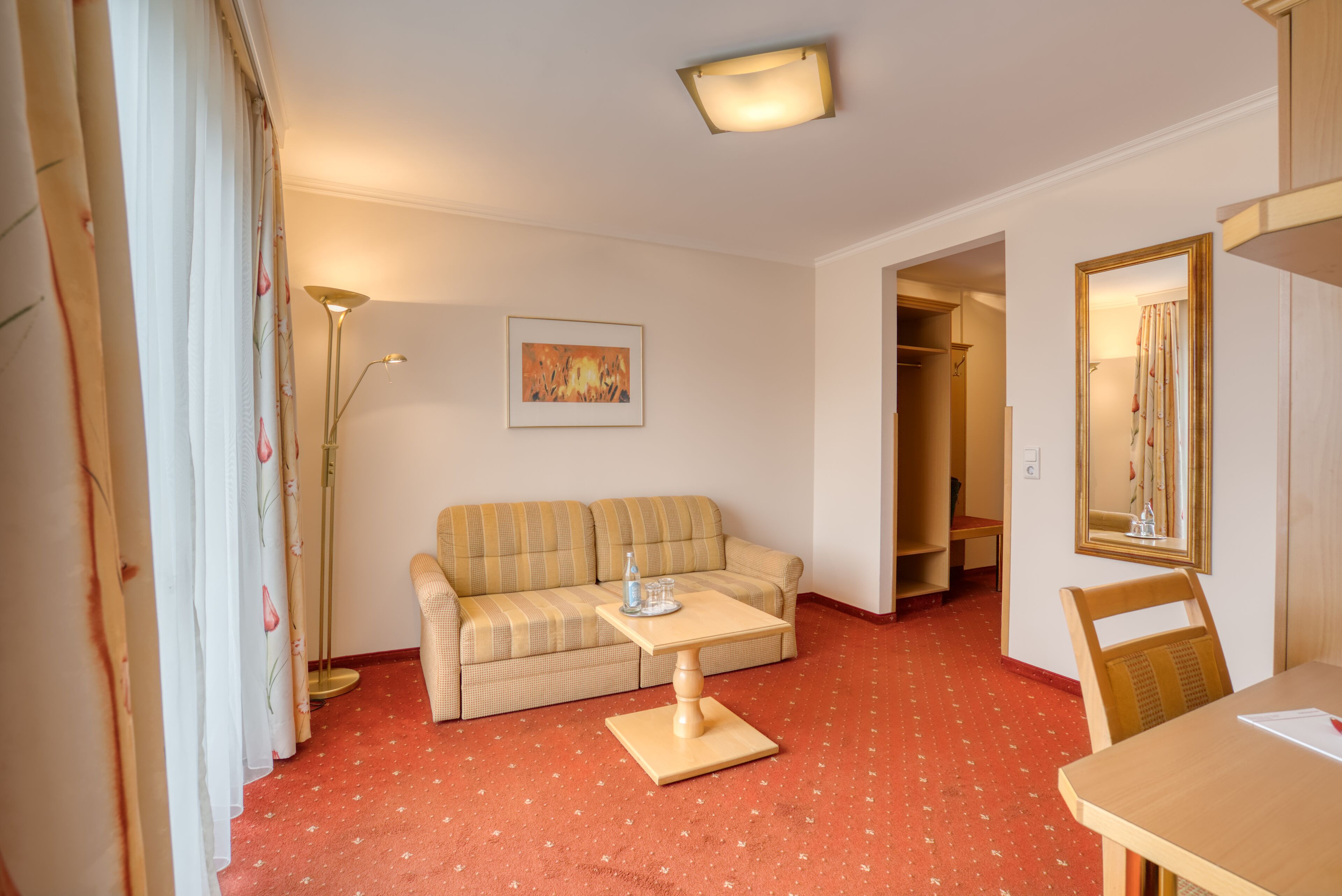 Ein Zimmer mit einer Couch, einem kleinen Tisch, einer Stehlampe und einem Bild an der Wand.