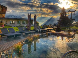 A pool area with lounge chairs, a wooden deck, and a mountain backdrop. - Schillerkopf Alpinresort (Buerserberg)