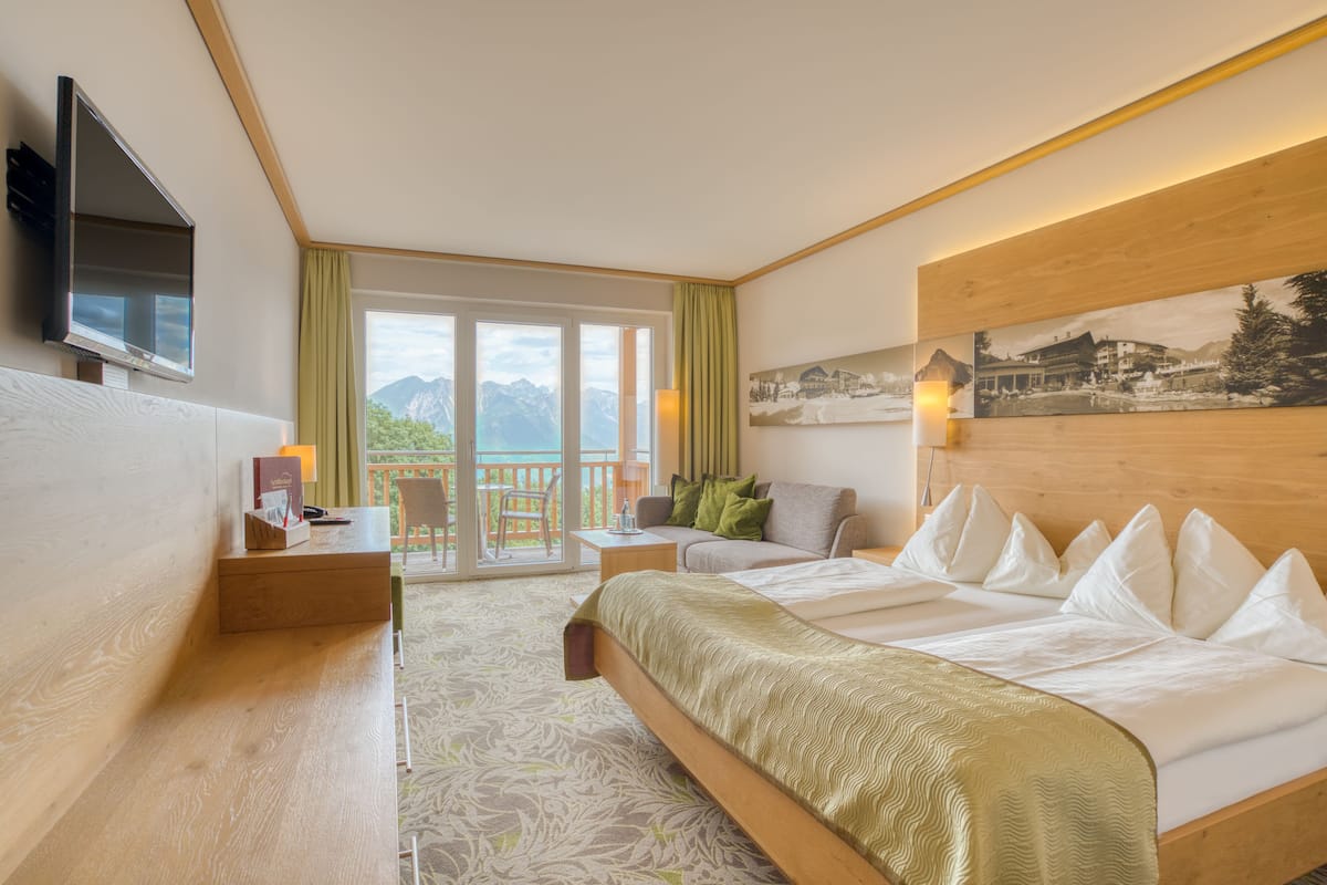 A hotel room with a bed, a television, a desk, and a view of mountains.