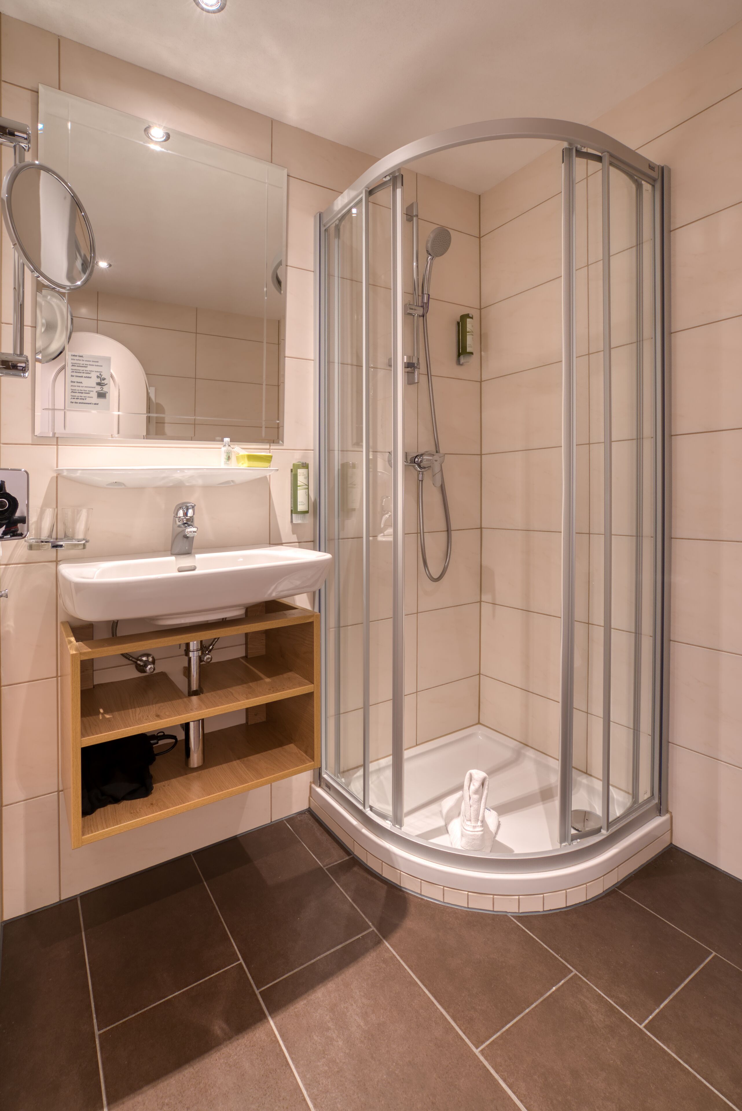 A modern bathroom with a glass-enclosed shower, a sink with a mirror, and a wooden shelf.