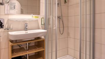 A modern bathroom with a glass-enclosed shower, a sink with a mirror, and a wooden shelf.