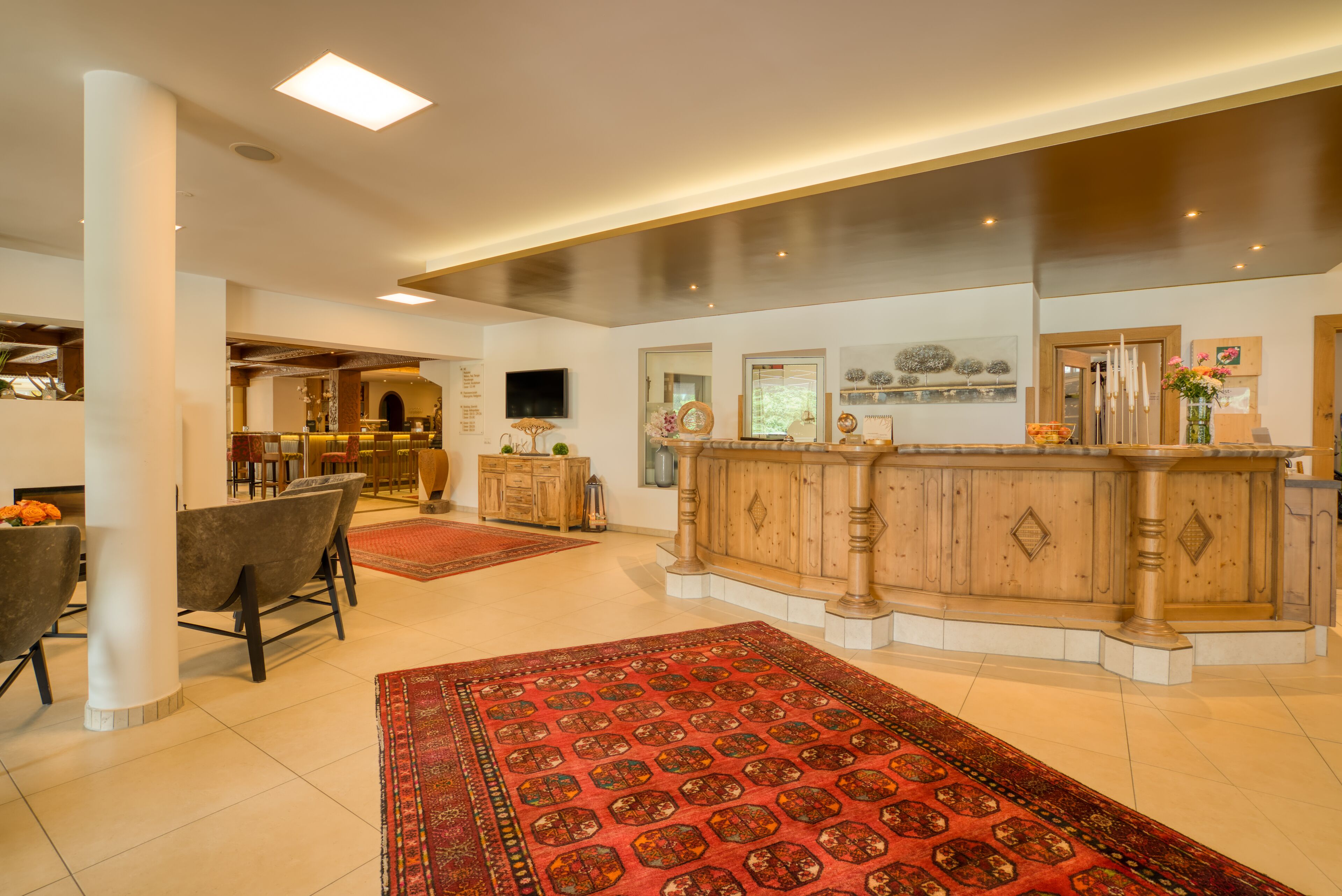 A spacious lobby with a wooden reception desk, comfortable seating, and a large red patterned rug.