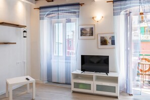 A modern living room with a flat-screen TV, a small white table, and a balcony with a railing. - Our delightful apartment is ideal for 4 people and is located in a privileged position at the small port of Riomaggiore, which gives its guests the opportunity to enjoy a fantastic experience in the heart of the 5Terre at its best!The characteristic terr (Riomaggiore)