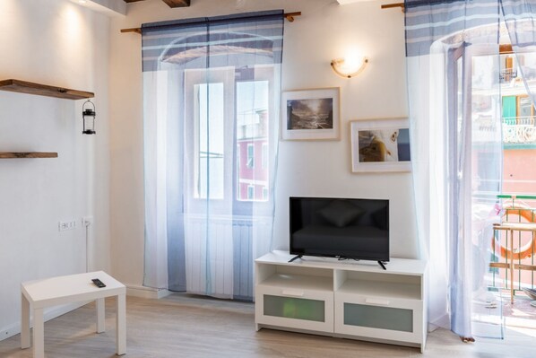 A modern living room with a flat-screen TV, a small white table, and a balcony with a railing.