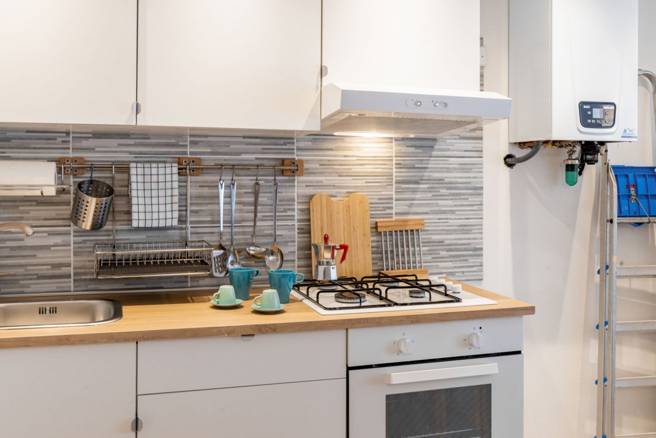 Una cucina moderna con mobili bianchi, piano cottura a gas, forno integrato e zoccolo rivestito in piastrelle.
