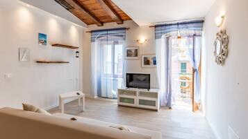 A living room with a sofa, TV stand, and a balcony with curtains.